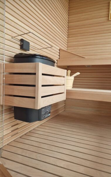 PARTICOLARE INTERNO DI SAUNA CON STUFA NERA E PROTEZIONE SOPRA STUFA